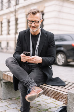 Stylish man seated on a city bench using a mobile
