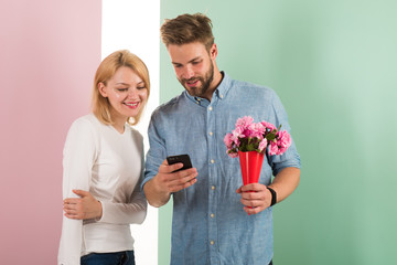 Guy with phone and bouquet of flowers, pastel pink and green background. Romantic concept. Couple...