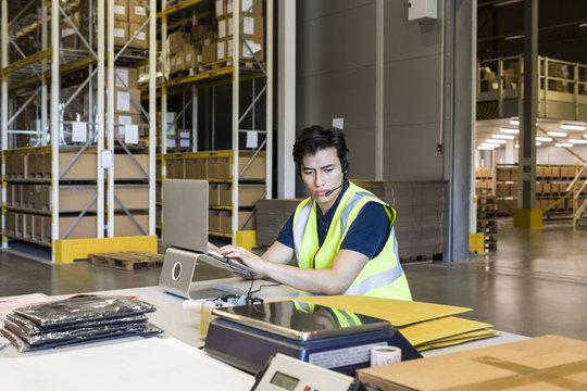 Confident young male customer service representative using laptop while sitting at desk in warehouse