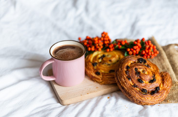 Close up of tasty and delicious breakfast in bed with cake and cacao. Fresh bake and coffee in pink cup on wooden board, near orange autumn berries. Concept of autumn morning.