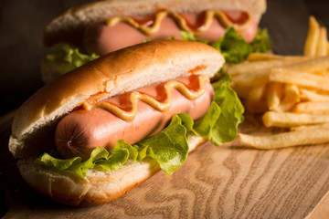 Photo of barbecue grilled hot dog with yellow mustard and ketchup on wooden background. Hot dog sandwich with potato fries and sauces.