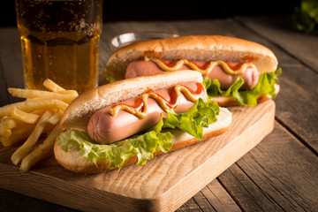 Photo of barbecue grilled hot dog with yellow mustard and ketchup on wooden background. Hot dog sandwich with potato fries and sauces.