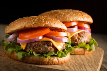 Home made hamburger with beef, onion, tomato, lettuce and cheese. Fresh burger close up on wooden rustic table with potato fries, beer and chips. Cheeseburger.