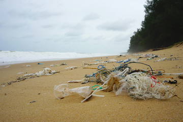 Plastic trash all over the beach with heavy wave and pine tree background
