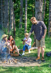 Tourists sharing thoughts about hike sit on log. Company having hike picnic nature background. Picnic with friends in forest near bonfire. Hikers sharing impression of walk forest. Summer tradition