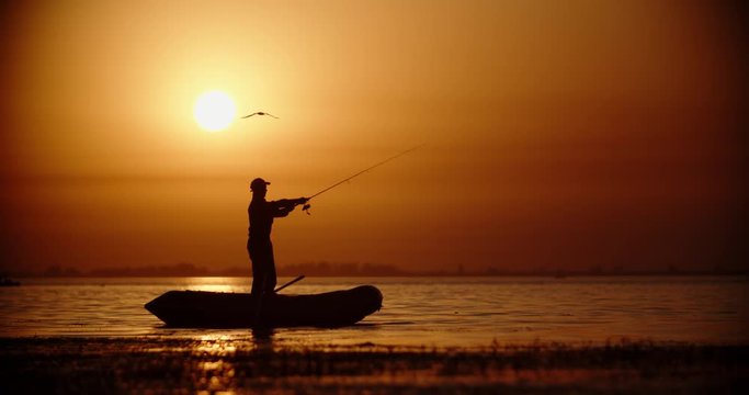 Professional fisherman trying to catch a fish with spinning rod in a rubber boat. lake in golden sunset 4k
