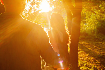 Handsome guy and brunette girl walking on the natural background on a beautiful warm sunset. boy leads the girl holding the hand