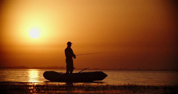 Professional fisherman trying to catch a fish with spinning rod in a rubber boat. lake in golden sunset 4k