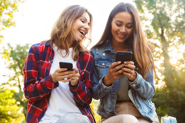 Women friends students walking in the park using mobile phone.