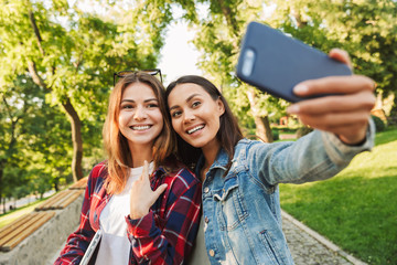 Beautiful ladies students walking in the park take a selfie by mobile phone.