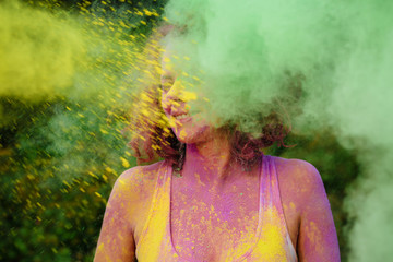 Pleased caucasian woman with curly hair posing in a cloud of green and yellow Gulal paint