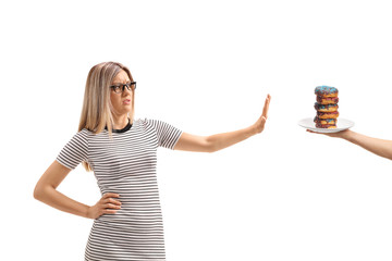 Young woman making a refuse gesture with her hand to a pile of donuts