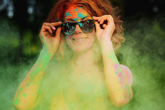 Emotional caucasian model wearing sunglasses, posing in a cloud of green Gulal paint