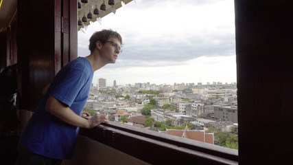 Fototapeta premium Young Man Looking Out Window With City in Background