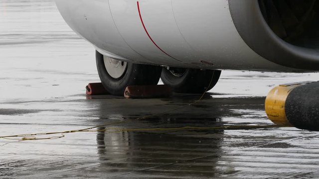 Chocked wheels of airplane undercarriage and part of jet engine under heavy rain