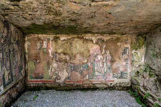 Flaking mosaic figures in a wet ancient roman cave wall.