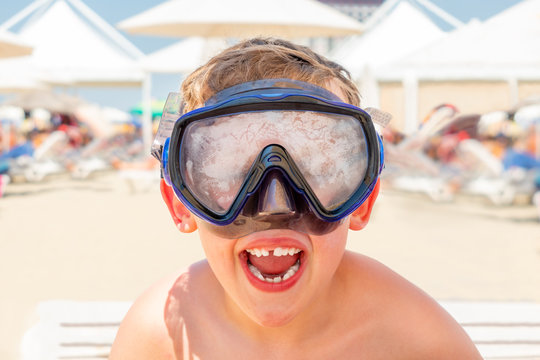 Closeup portrait of a happy laughing boy with diving mask at a sunny beach.