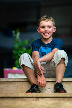 Portrait of a happy smiling young boy sitting on stone stairs outdoors at night.