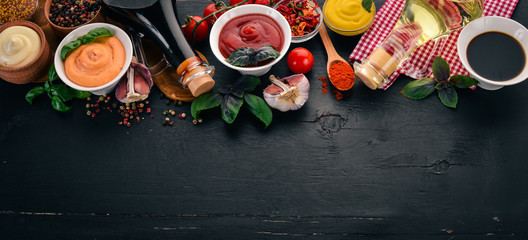 Set the sauces on a black wooden background. Ketchup, mayonnaise, mustard, soy sauce, barbecue sauce, pepper and spices. Top view. Free space for text.