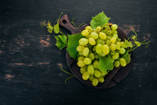 Fresh green grapes with leaves of grapes. Top view. On a black wooden background. Free space for text.
