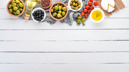Green olives and black olives, oil, bread, cheese and snacks. Italian cuisine. On a white wooden table. Top view. Free space for text.