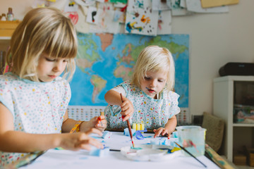 Portrait of happy adorable little girls painting at home together.