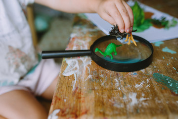 Portrait of adorable little girl playing magnifying glass at home looking at artificial plants and toys.