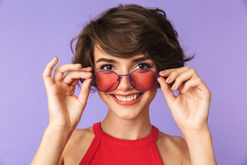 Image of cheerful woman 20s in casual wear and sunglasses looking at you with smile, isolated over violet background