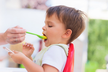 Baby eating the lunch while looking at the smartphone