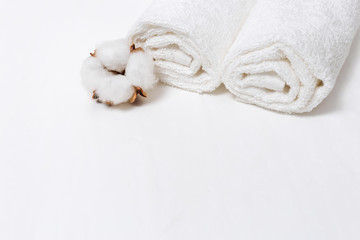 White flower of cotton plant  and two white cotton towels on white concrete background with copy space. Spa set.