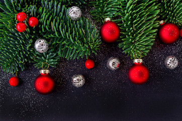 christmas decoration with fir tree branch, red berrys and baubles, on black background closeup