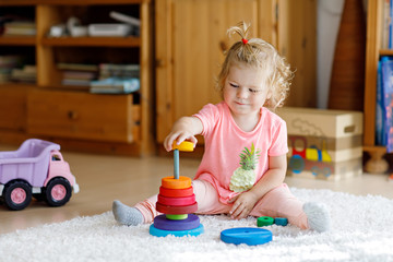 Adorable cute beautiful little baby girl playing with educational colorful wooden rainboy toy pyramid