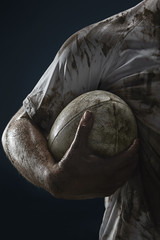 Rugby player hands with ball on dark background. Close up