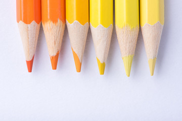 Macro photograph of several pencils of yellow and orange color on a white background