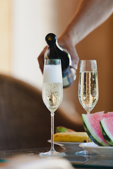 Hand pours champagne into tall glasses