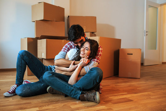 Young couple moving into a new home.They sitting on floor in empty apartment .Real estate concept.Embrace each other.
