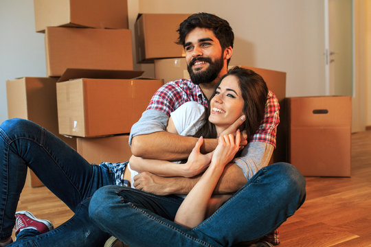 Young couple moving into a new home.They sitting on floor in empty apartment .Real estate concept.Embrace each other.