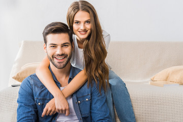 portrait of young smiling couple looking at camera on sofa at home