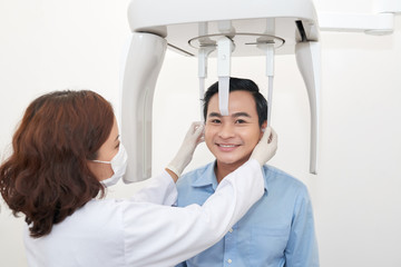 Smiling Asian man in dentist office having procedure of panoramic dental radiograph with doctor and special equipment