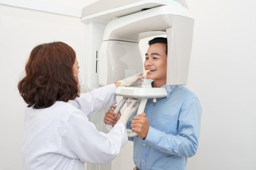 Professional dentist using special equipment and making panoramic dental x-ray of smiling Asian man in office