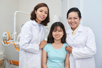 Fototapeta premium Cheerful Asian dentists and charming girl in modern dental office smiling happily at camera