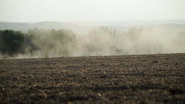 Traktor auf Feld wirbelt Staub auf, Mittelgebirgslandschaft und B&auml;ume im Hintergrund