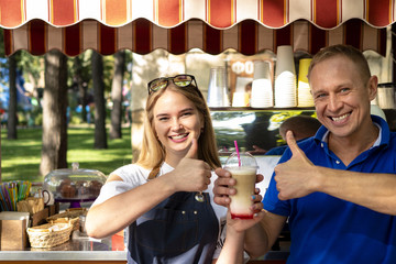 Man and woman barista with a glass of coffee in the park. Mobile coffee cart in the park - obrazy, fototapety, plakaty