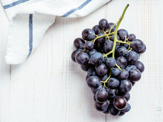 Bunch of dark organic ripe grapes on white wooden table with linen napkin or kitchen towel textile....
