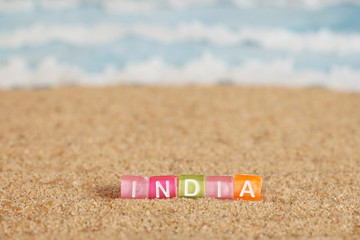 Word INDIA from multicolored cubes in the sand on the background of beach and sea