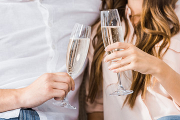 cropped shot of couple clinking glasses of champagne on sofa at new home