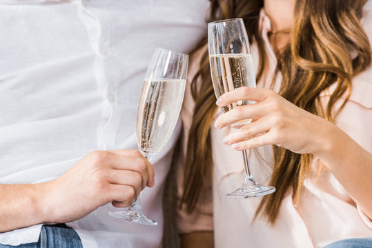 Cropped Shot Of Couple Clinking Glasses Of Champagne On Sofa At New Home