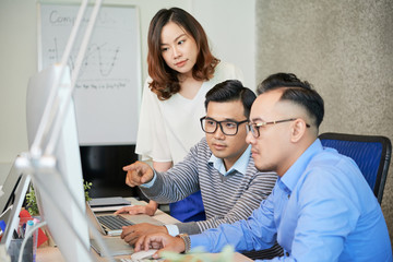 Group of Asian men and woman at table in modern office watching computer and talking about project 