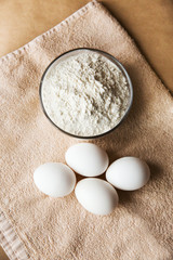 white chicken eggs and bowl with flour on brown tablecloth