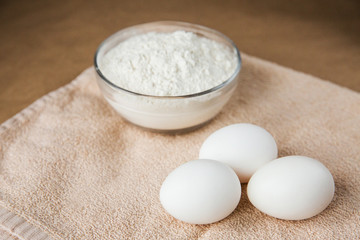 white chicken eggs and bowl woth flour on brown tablecloth